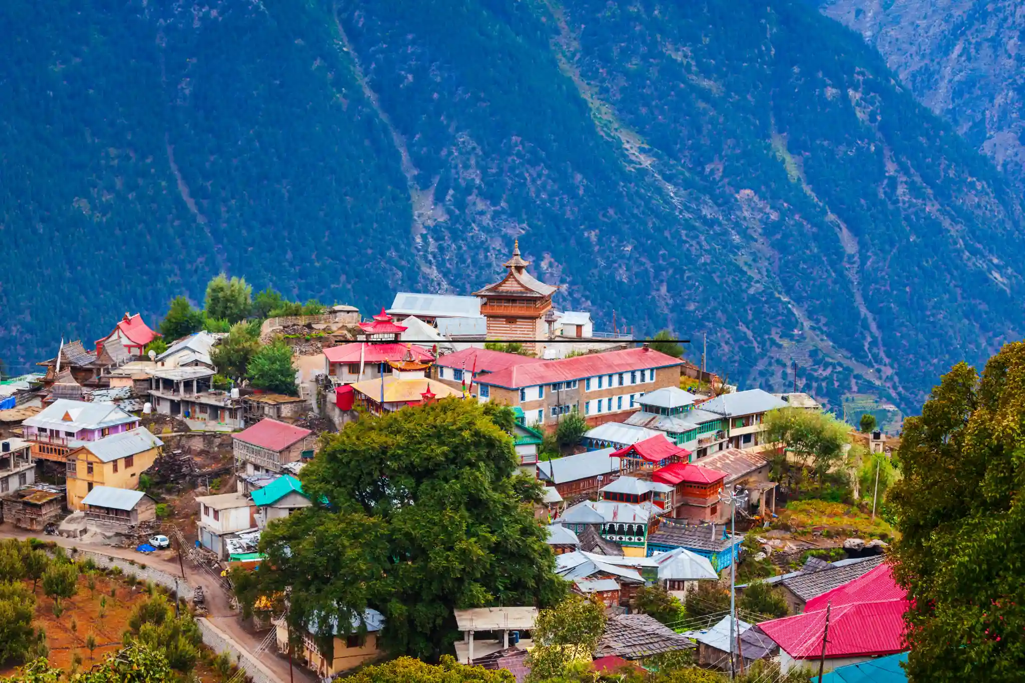 Scenic view of a colorful Himalayan village surrounded by lush greenery and majestic mountains in Manali, Himachal Pradesh.
